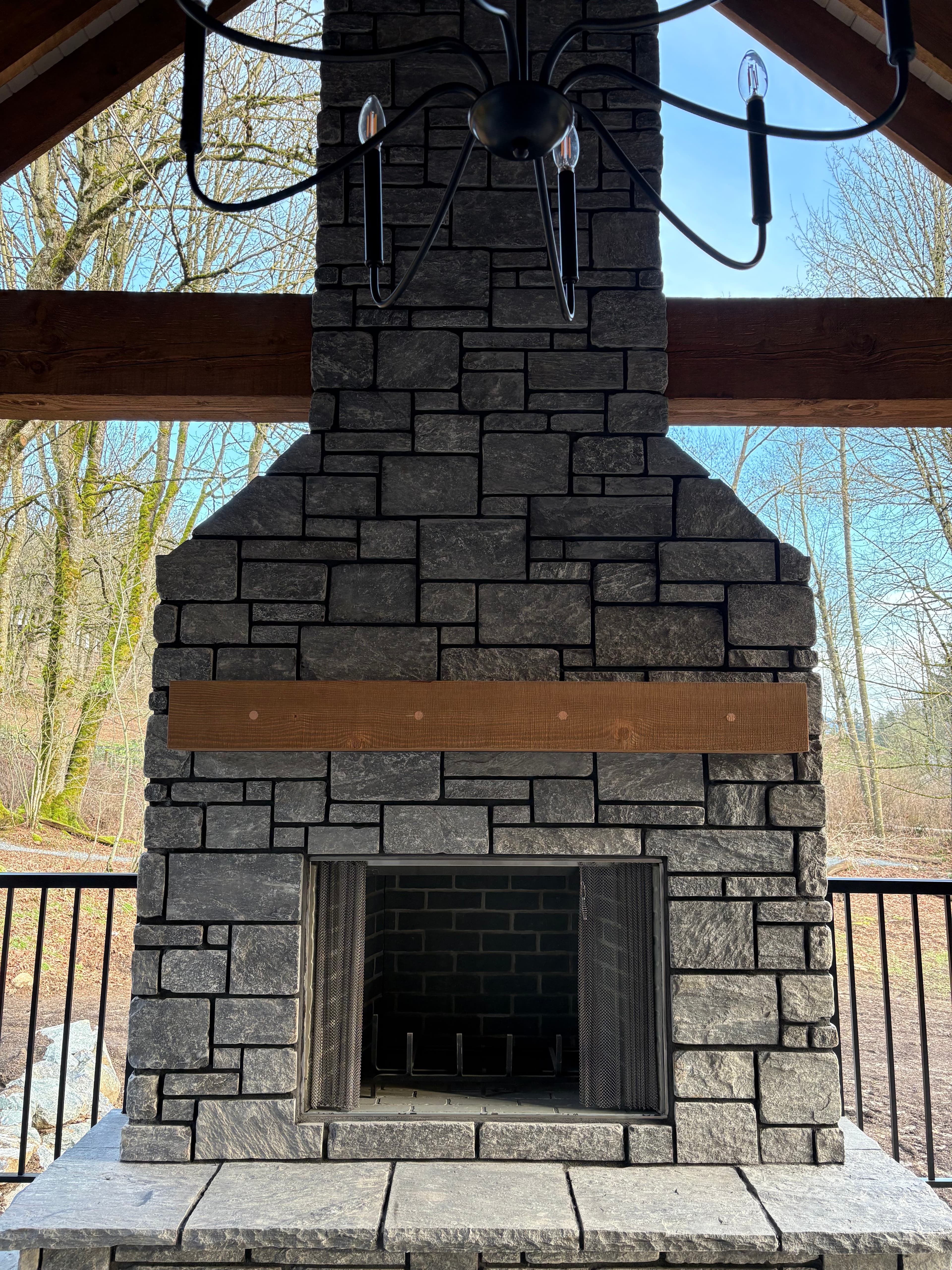 Built outdoor stone fireplace with firebox and stone hearth under a covered porch